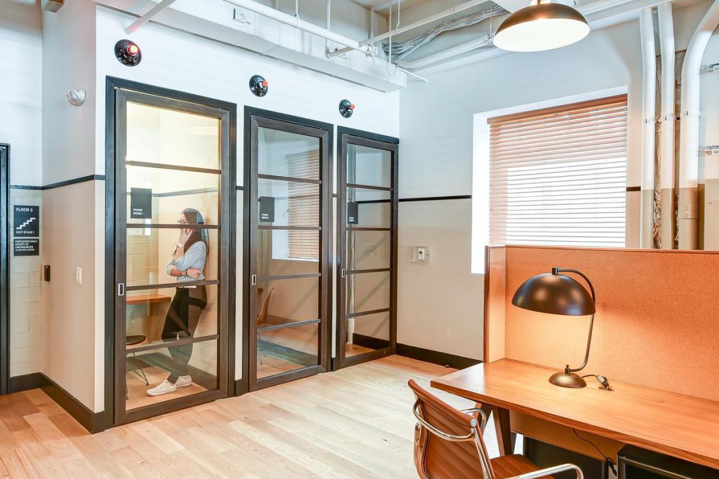 A modern office space includes open-concept desk areas and private, single-person booths for more focused work.