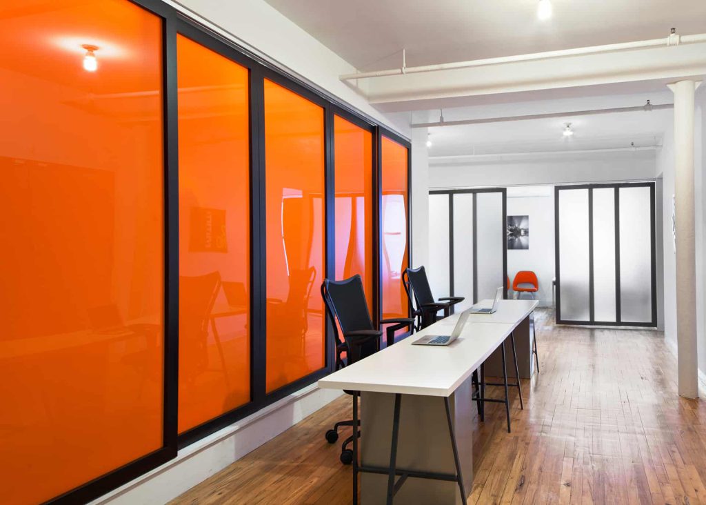 This office space includes a vibrant room divider with bright-orange inserts, which also offer complete visual privacy for the neighboring space.