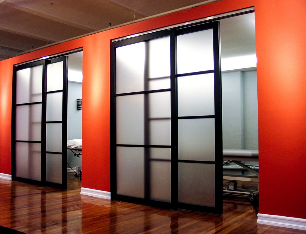 Two slightly ajar sliding door systems reveal private medical office spaces for appointments. A brightly painted wall adds a pop of style to the room.
