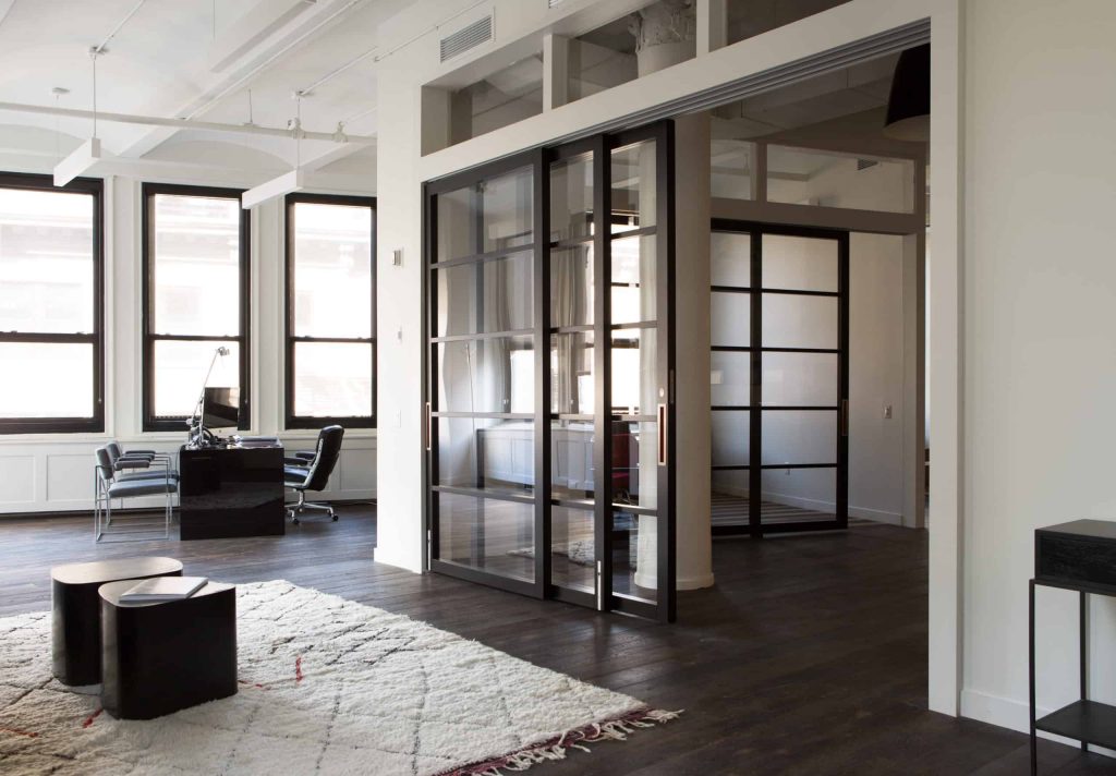 A modern office environment features group workstations, social gathering space, and a partitioned meeting area.