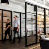 Two people walk through a hallway that is divided by a series of sleek, black-framed sliding doors.