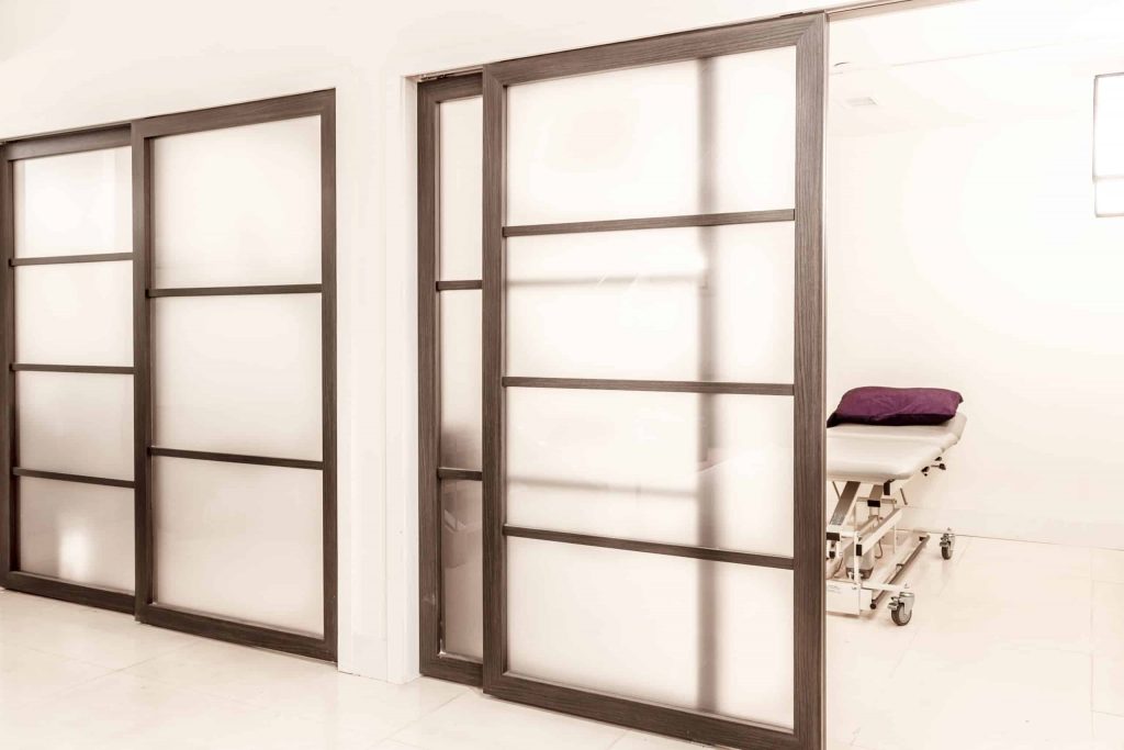 Two sets of translucent, sliding doors are used to segment private rooms from the rest of a physical therapy clinic.