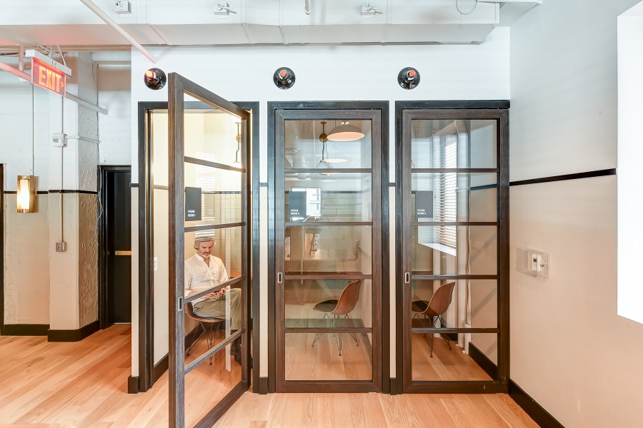 Three swinging doors with one opened into an office where someone is working.