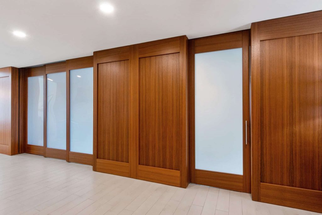 A spacious hotel suite featuring large glass sliding doors that separate the bedroom from the bathroom area. The warm wood tones of the doors add a touch of elegance and create a seamless, cohesive look in the contemporary suite.