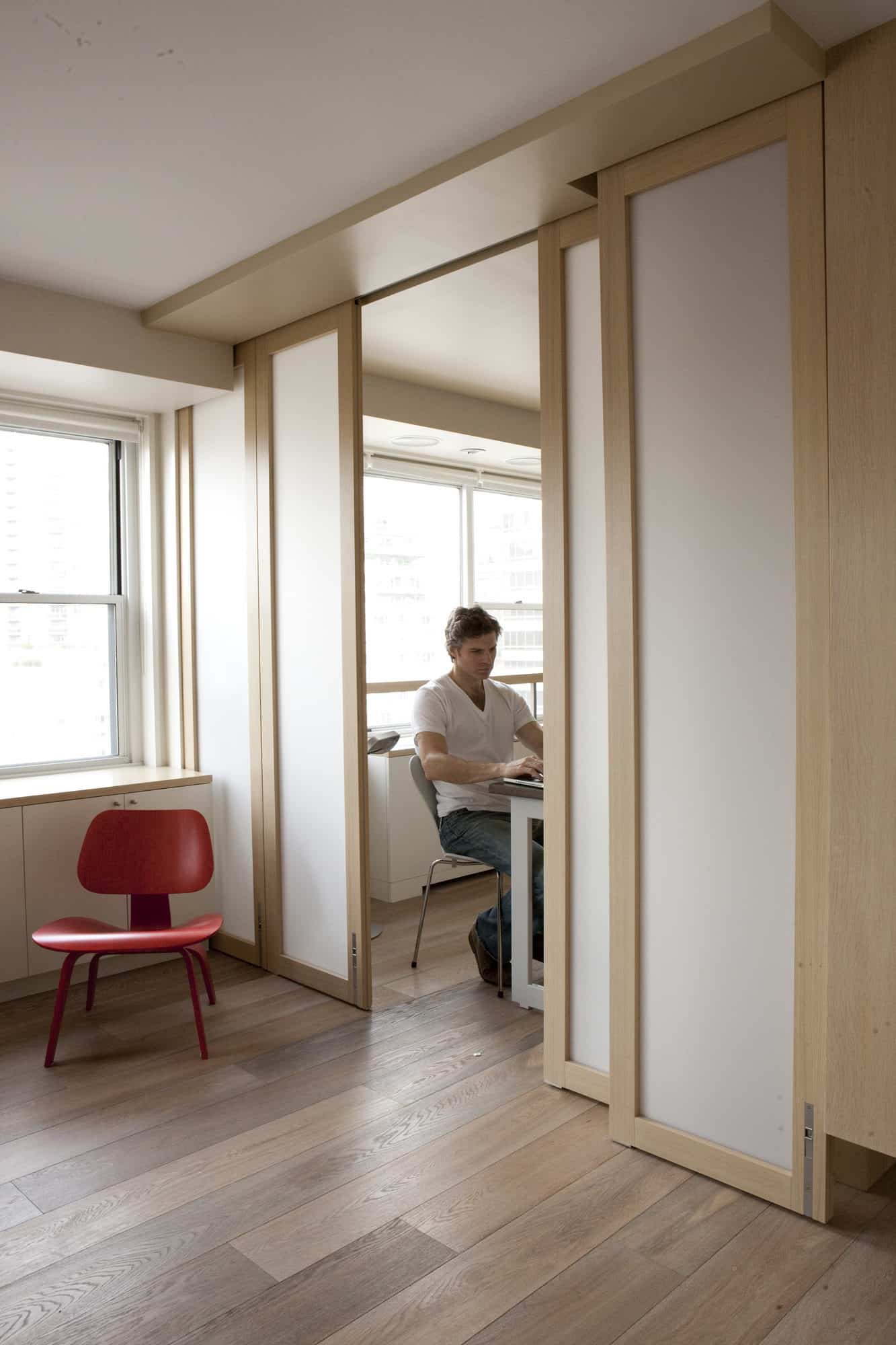 Opaque light wooden stacking doors opened into an office with a man working at a desk.