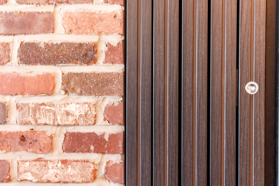 Dark wooden wing door on a red brick wall.
