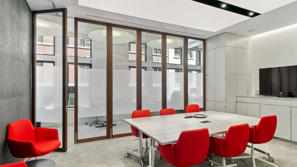 This conference room is furnished with stylish, red chairs, a TV station, and a large operating wall system.