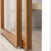 Close-up of the bottom of a wooden-framed glass sliding door, highlighting the craftsmanship of the frame and the smooth sliding mechanism. The door's glass panels reflect light, complementing the light-toned flooring in the modern interior.