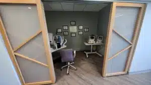 The testing room of a medical office with light wood and frosted window sliding privacy doors open.
