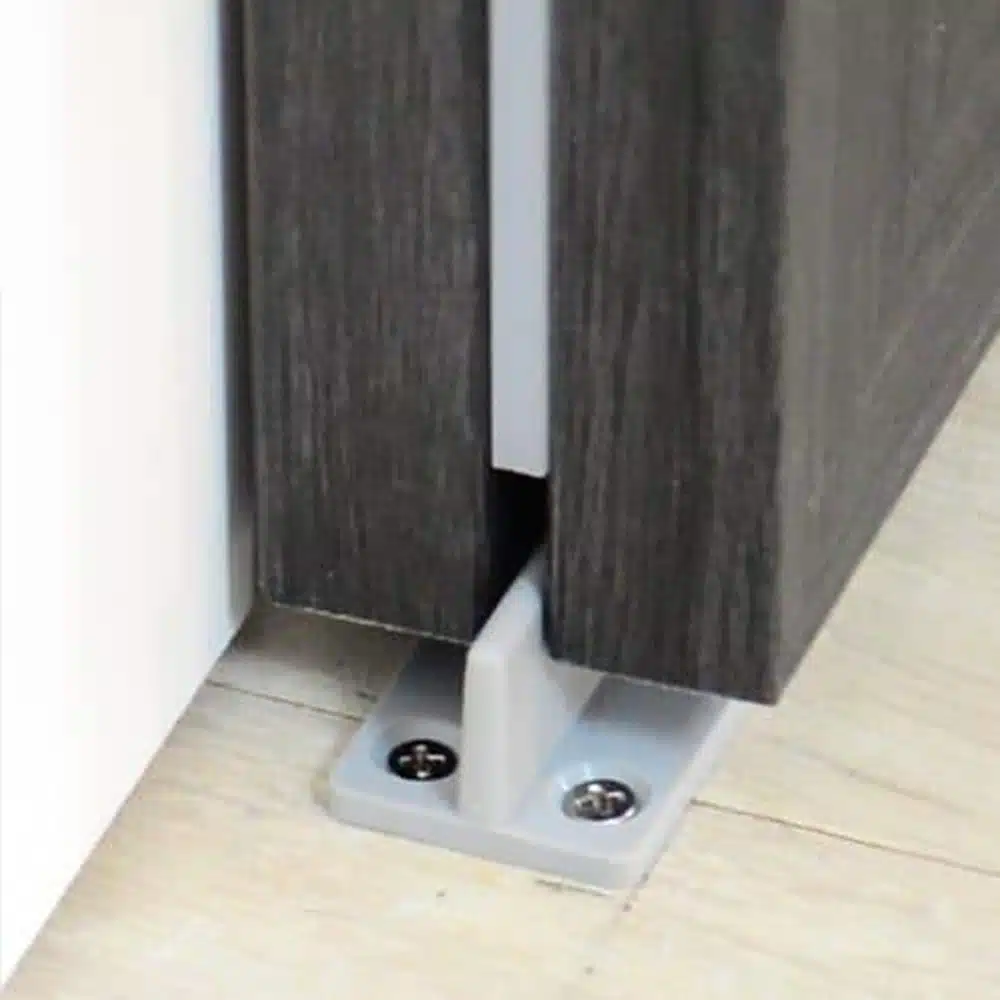 Raydoor sliding door floor guide mounted on wood flooring, stabilizing a dark wood door panel for smooth operation.